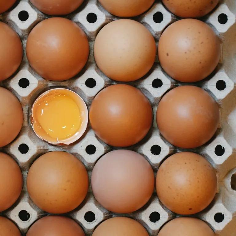A carton of brown eggs with one cracked open showing the yolk